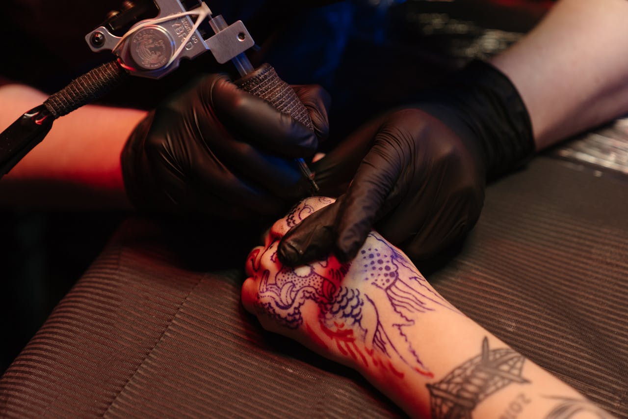 A tattoo artist wearing black gloves working on a detailed dragon design in a studio.