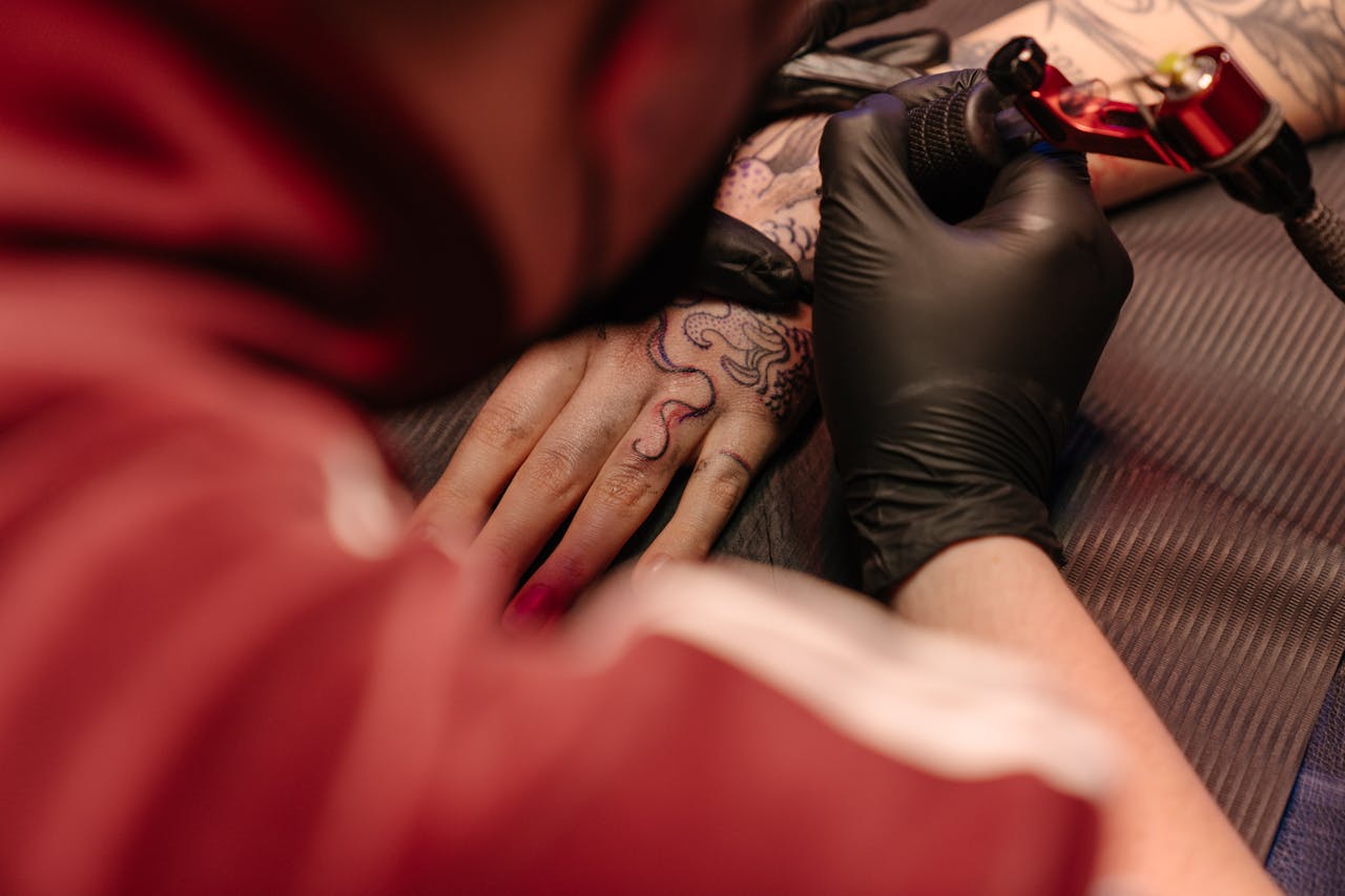 Tattoo artist working on client's hand with black gloves in a studio environment.